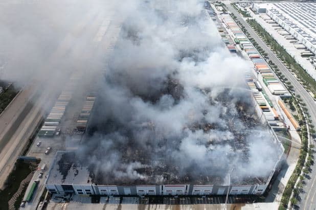 Aerial view of a massive California warehouse fire with thick smoke rising as the suspect reportedly invokes Luigi Mangione in an anti-corporate statement.
