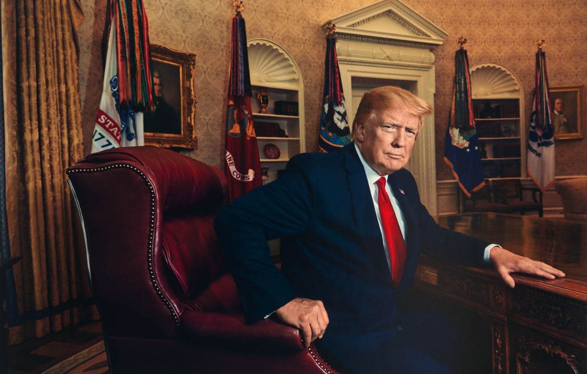 Donald Trump seated in a formal office setting with American flags and presidential decor in the background