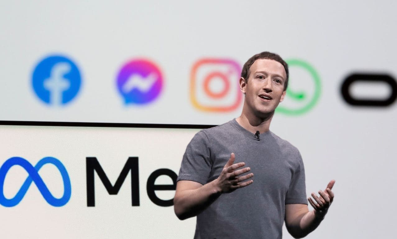 Mark Zuckerberg speaking on stage with Meta logo and Facebook, Messenger, Instagram, and WhatsApp icons in the background