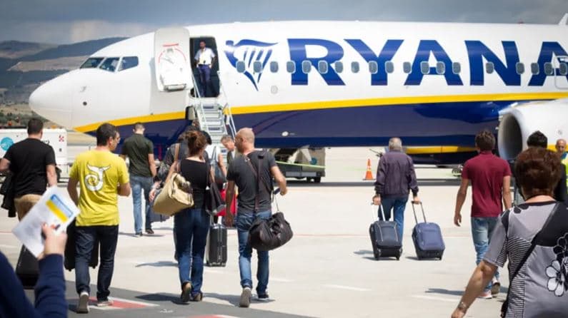Passengers boarding a Ryanair aircraft after the airline reported a 34% profit decline due to higher jet fuel costs.